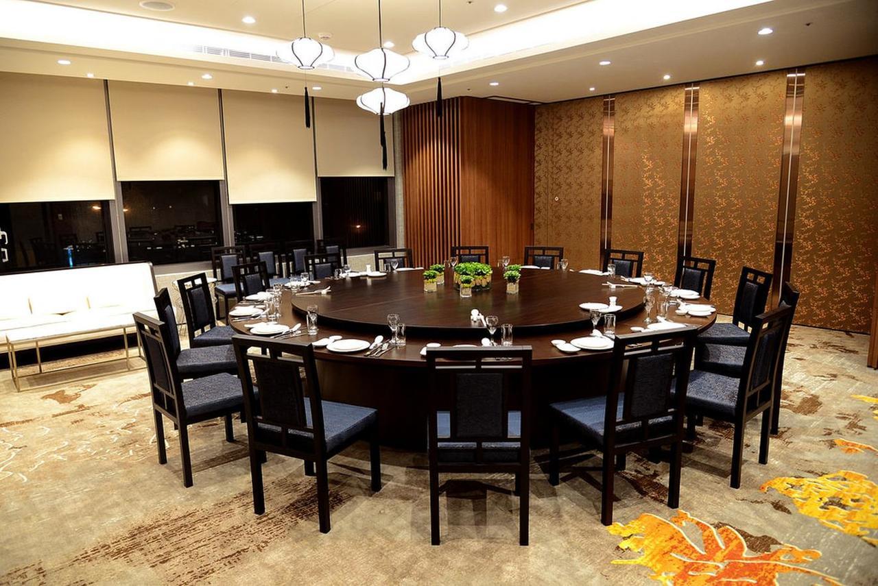 Caesar Metro Taipei Hotel Bagian luar foto The photo shows a large, elegantly set dining room with a circular table surrounded by black chairs. The table is equipped with plates, utensils, and glassware, suggesting it's prepared for a formal meal. The room features modern lighting fixtures ha