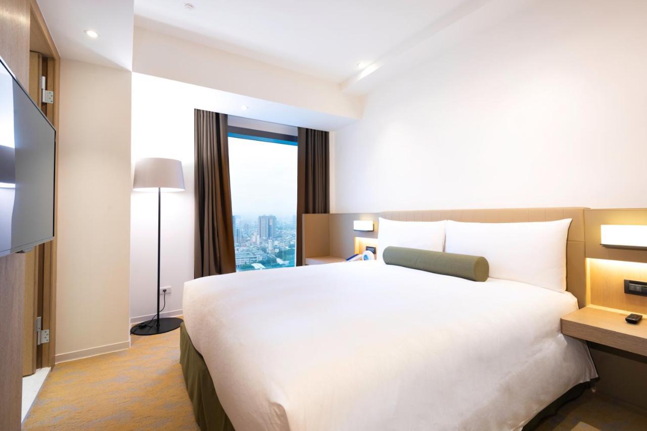 Caesar Metro Taipei Hotel Bagian luar foto The photo shows a modern hotel room with a simple and clean design. It features a double bed with white bedding and a green accent pillow. There are two large windows with dark curtains, allowing natural light to enter. A floor lamp stands beside the